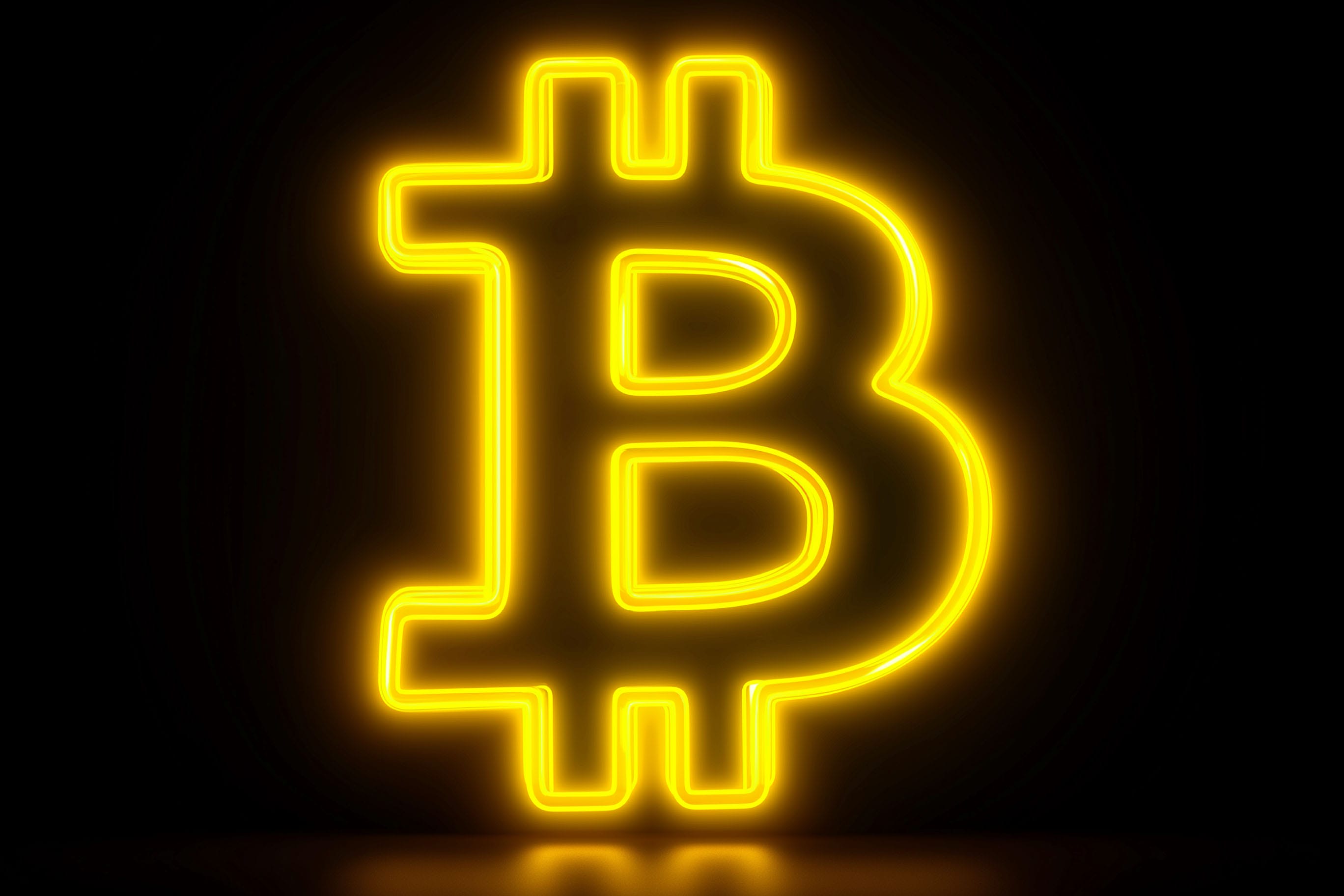 A bright yellow neon sign of the Bitcoin logo mounted on a dark brick wall, casting a warm glow.