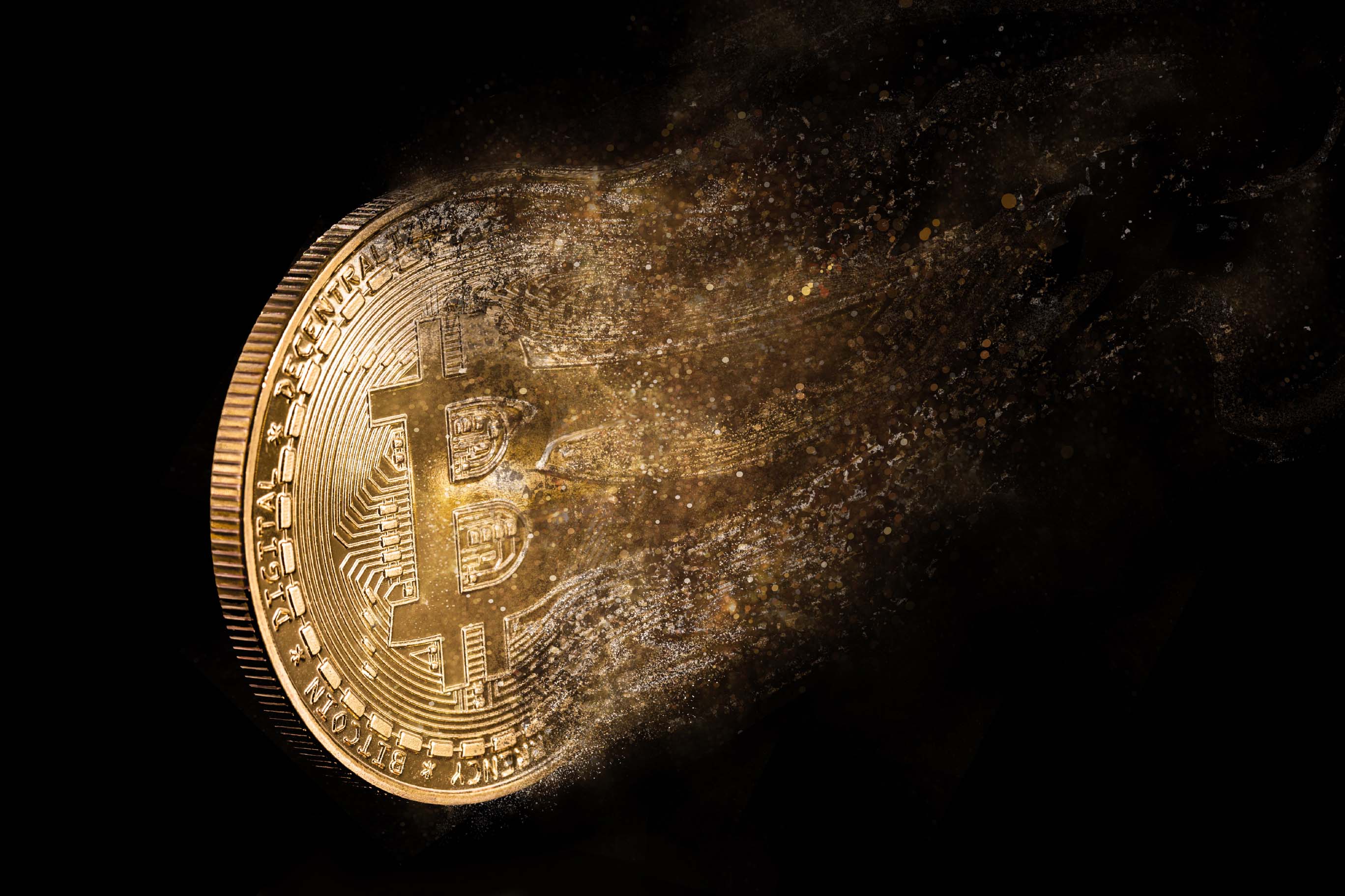 A golden Bitcoin coin set against a black background, with its right side dissolving or disintegrating into a cloud of small particles.