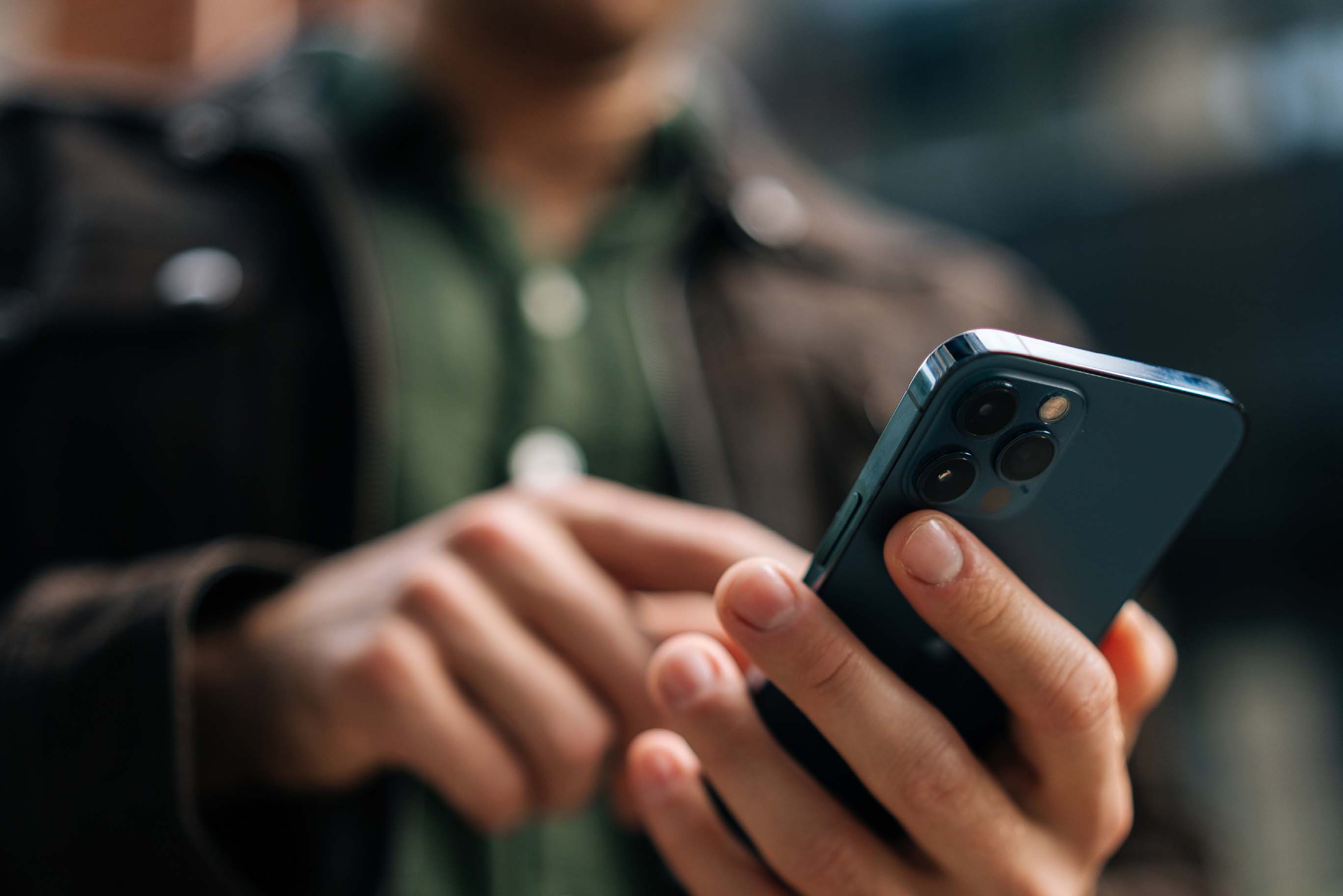 A close-up of a person's hands holding and using a blue smartphone, with their finger tapping the screen.