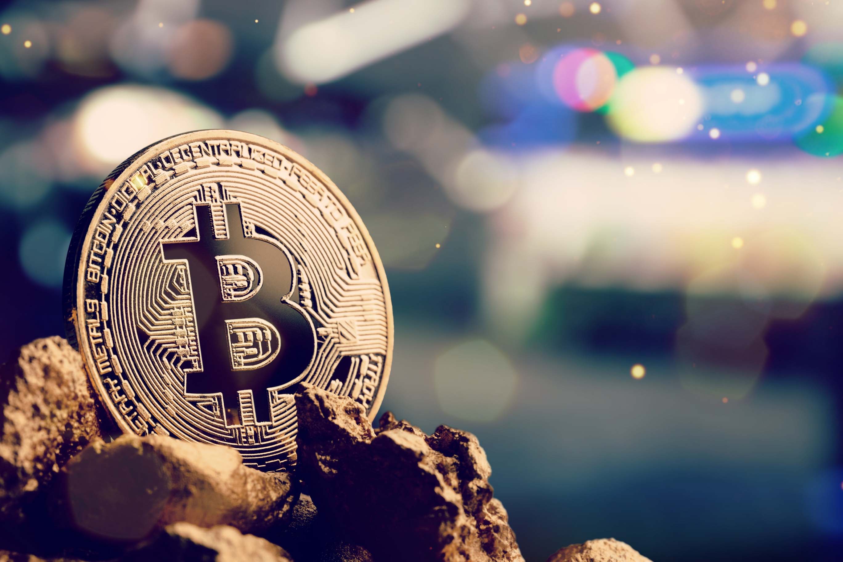 A stylized Bitcoin coin sitting on a rock with an out of focus background.